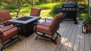 An outdoor patio with a grill, a table with chairs, and a patterned rug.