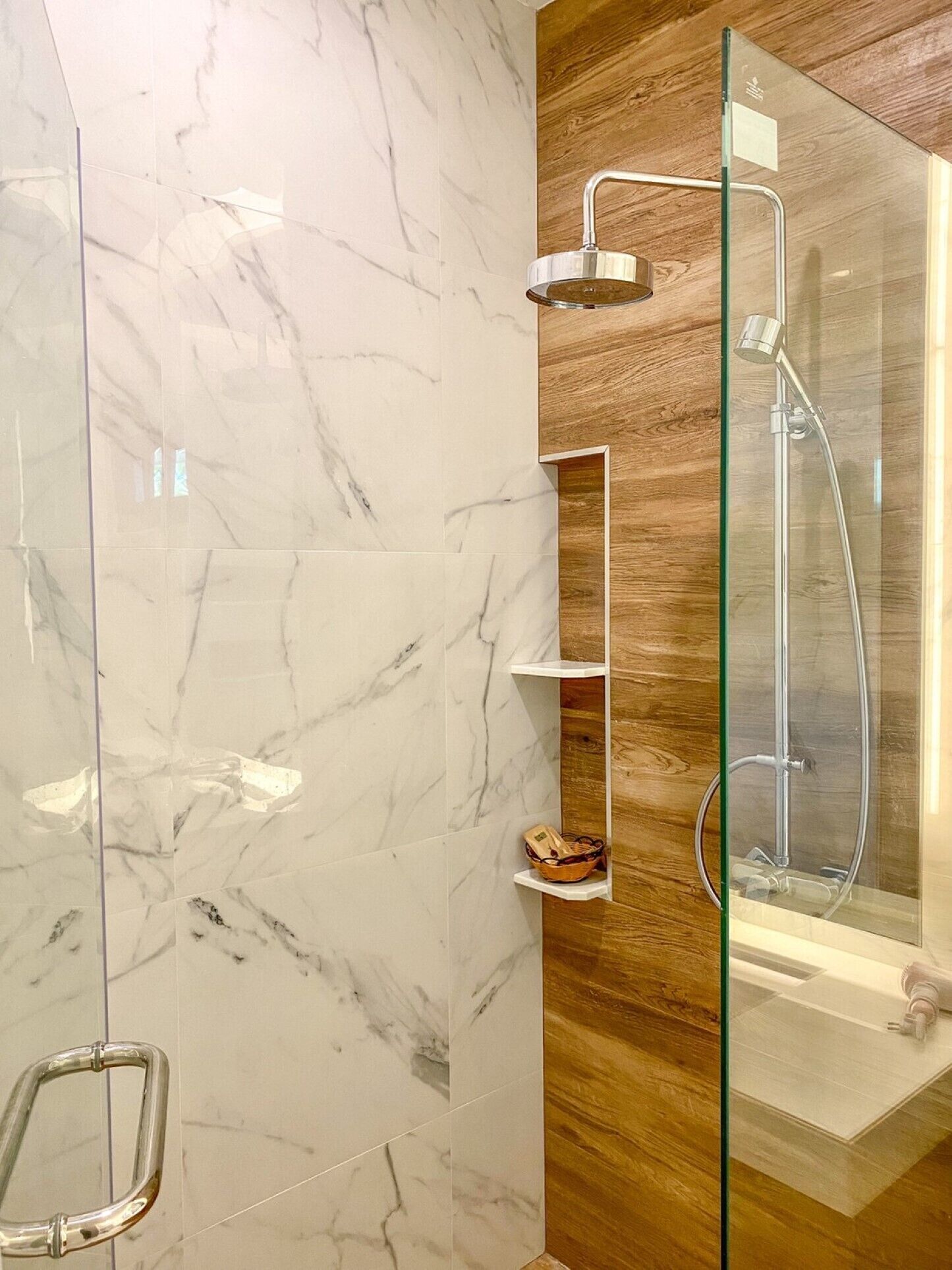 A modern bathroom with marble tiles, a glass shower enclosure, and wooden accents.