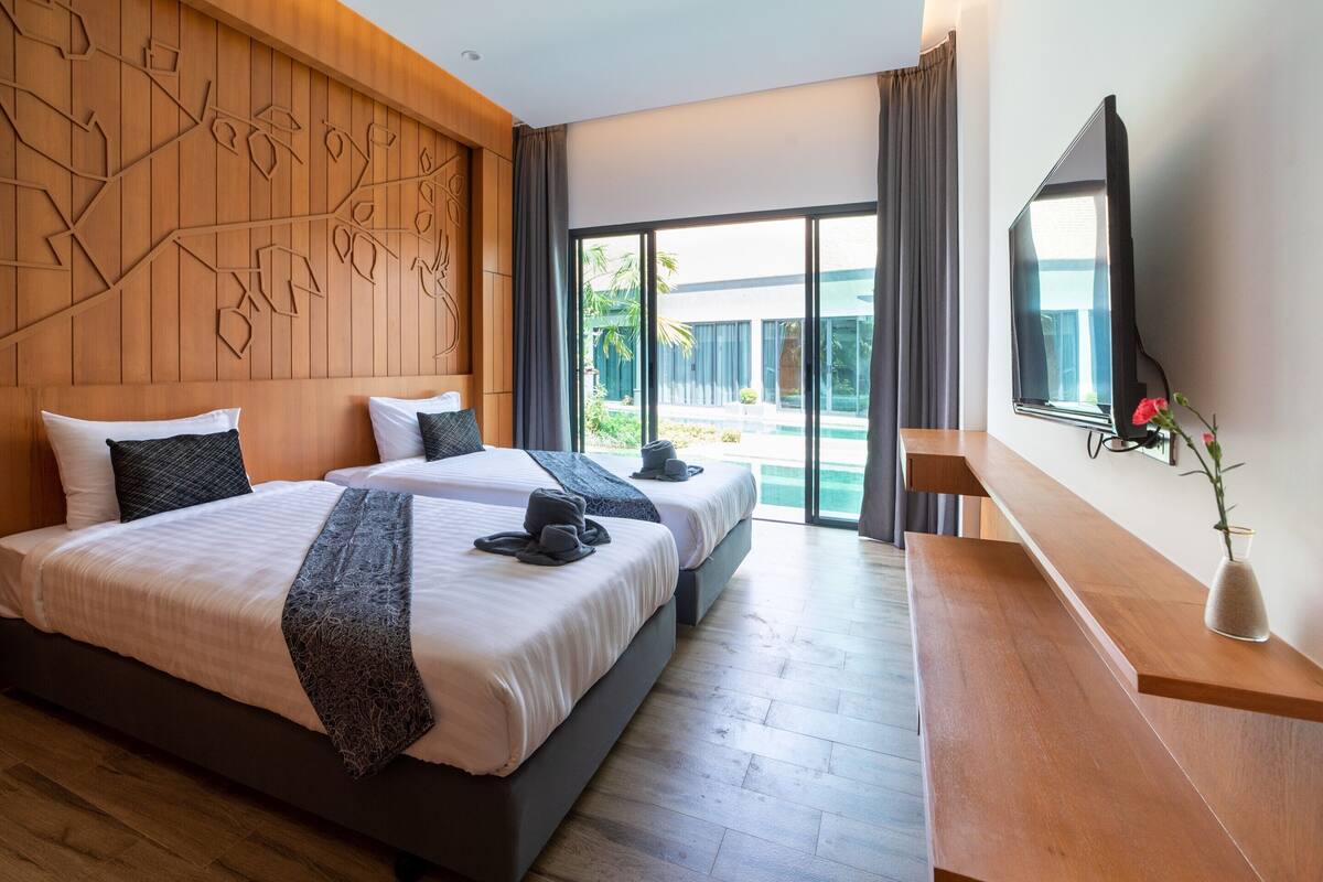 A hotel room with two beds, a wooden headboard, a large window, and a flat-screen TV.
