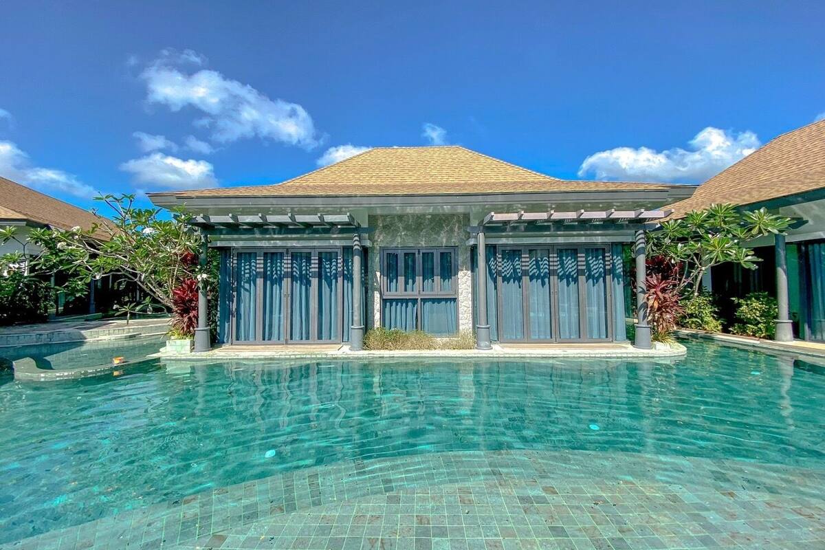 A modern resort with a clear swimming pool, two-story buildings with large windows, and tropical landscaping.