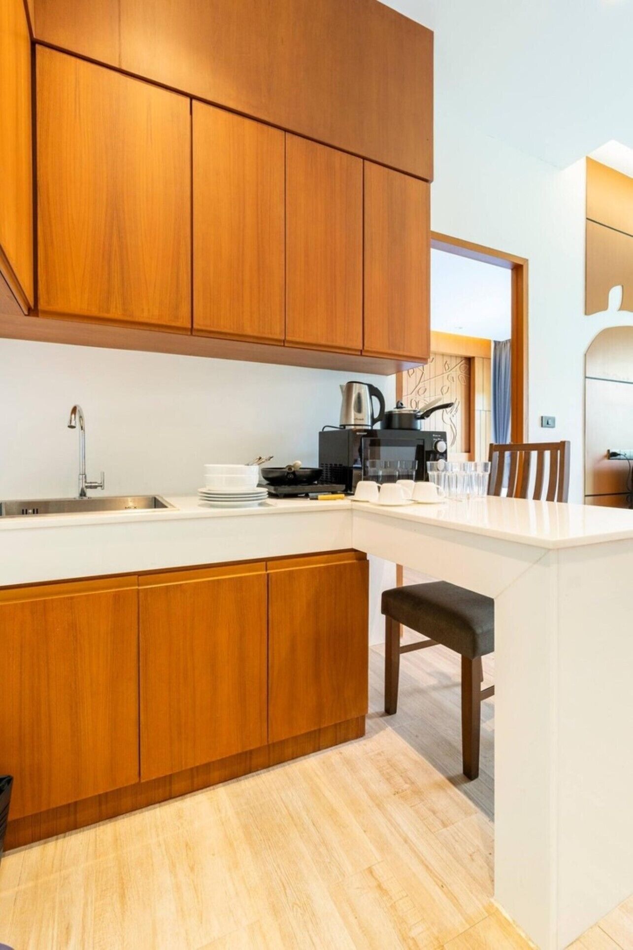 A modern kitchen with wooden cabinets, a white countertop, a coffee maker, and a dining area with a chair.