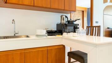 A modern kitchen with wooden cabinets, a white countertop, a coffee maker, and a dining area with a chair.