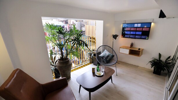 A modern living room with a brown leather sofa, a wooden coffee table with a remote control, a black chair, and a TV mounted on the wall. - Banana Inn Hostel (Hanoi)