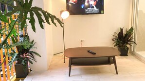 A living room with a TV mounted on the wall, a coffee table, and potted plants. - Banana Inn Hostel (Hanoi)