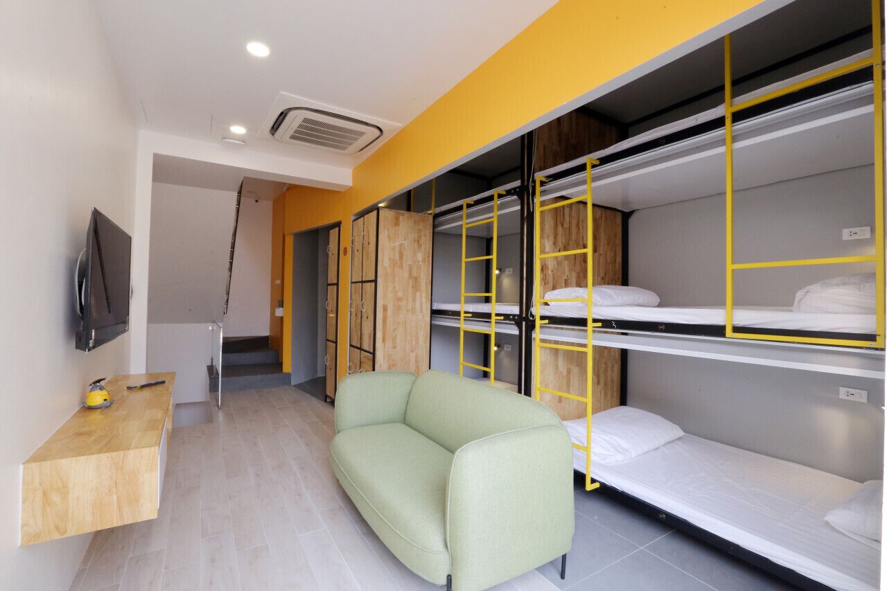 A compact room with bunk beds, a small sofa, a wooden desk, and a flat-screen TV.