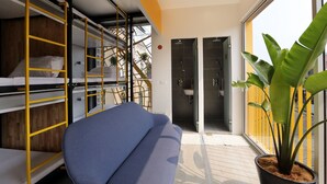 A room with bunk beds, a blue sofa, a potted plant, and a bathroom with a shower and sink. - Banana Inn Hostel (Hanoi)