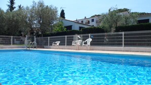 Una piscina con agua azul cristalina, rodeada por una cerca blanca y varias sillas de plástico blancas.