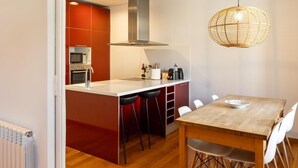 Une cuisine moderne dotée d’un îlot central, de meubles de rangement rouges et d’un coin repas avec une table en bois et des chaises blanches.