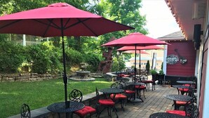 An outdoor patio area with multiple tables and chairs, red umbrellas, and a stone wall. - Historic Boutique Hotel (Branson)