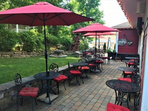 An outdoor patio area with multiple tables and chairs, red umbrellas, and a stone wall. - Historic Boutique Hotel (Branson)