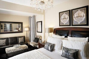 A hotel room with a large bed, a sofa, a chair, and a chandelier. - Historic Boutique Hotel (Branson)