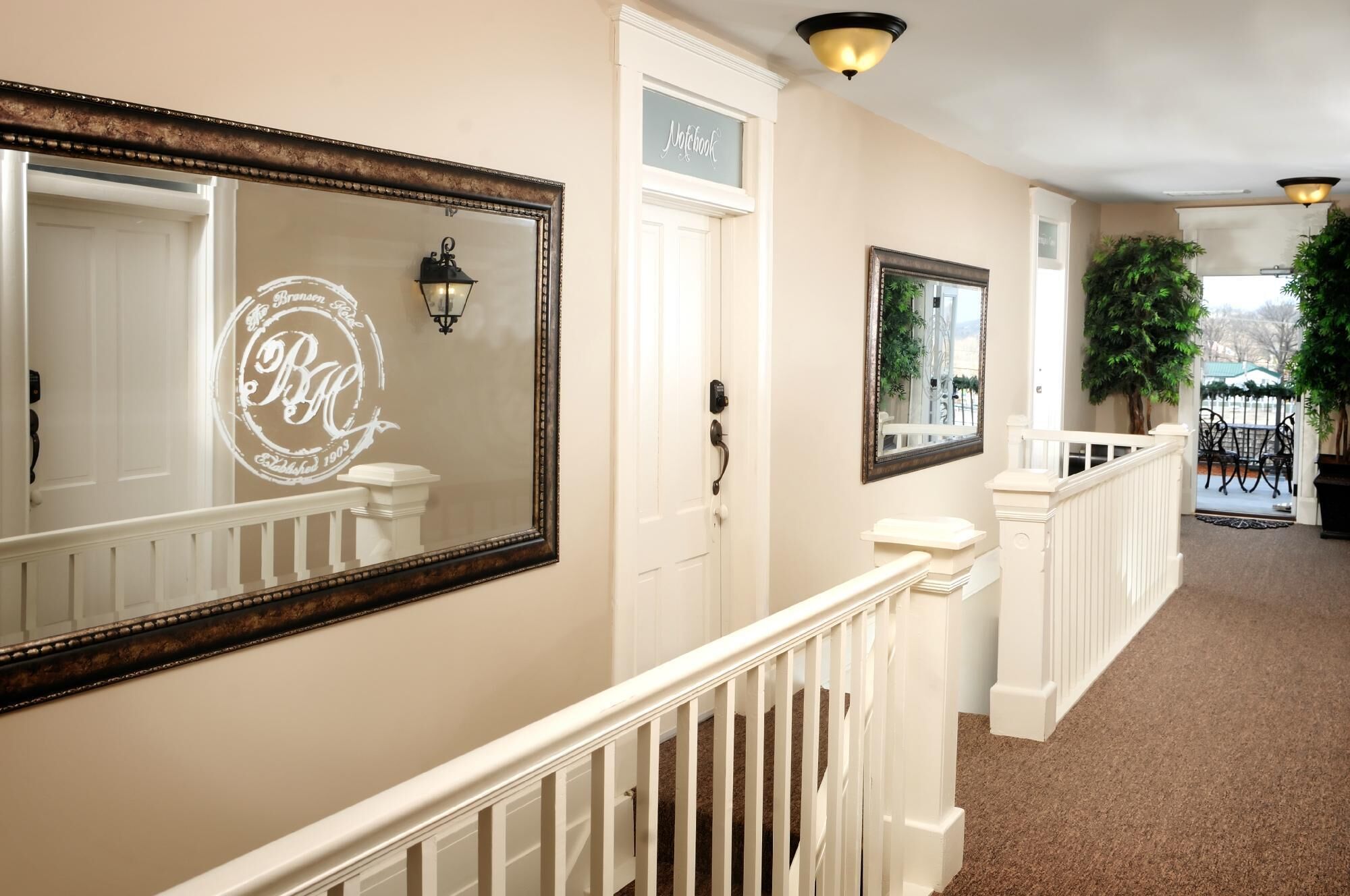A hallway with a white door labeled "Notebook," a large mirror with a decorative frame, and a potted plant.