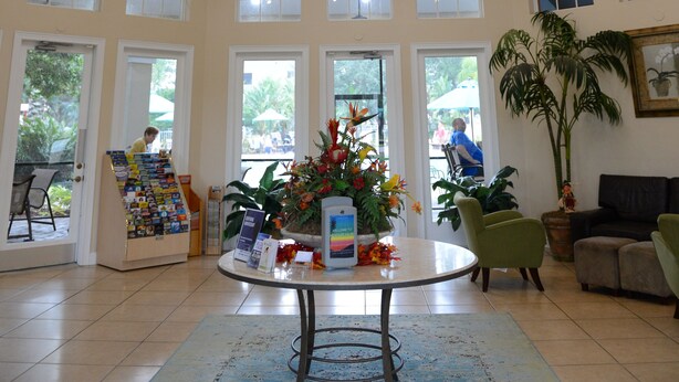 A spacious lobby with a high ceiling, large windows, and a central table with a floral arrangement.