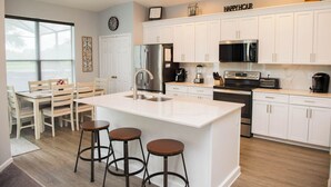 A modern kitchen with white cabinetry, stainless steel appliances, and a central island with stools.