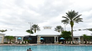 A swimming pool area with lounge chairs and umbrellas, a covered pavilion, and palm trees.
