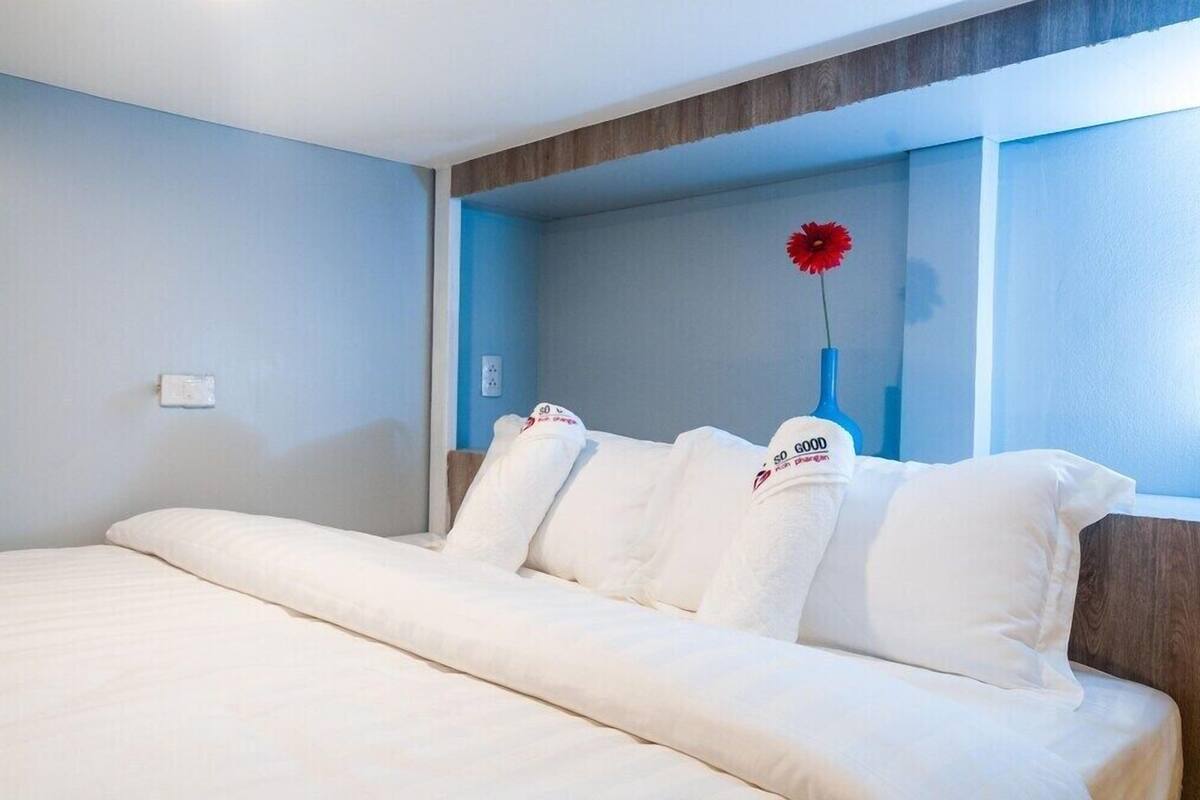 Une chambre d’hôtel avec un lit, des oreillers, une table de chevet et un vase contenant une fleur rouge.