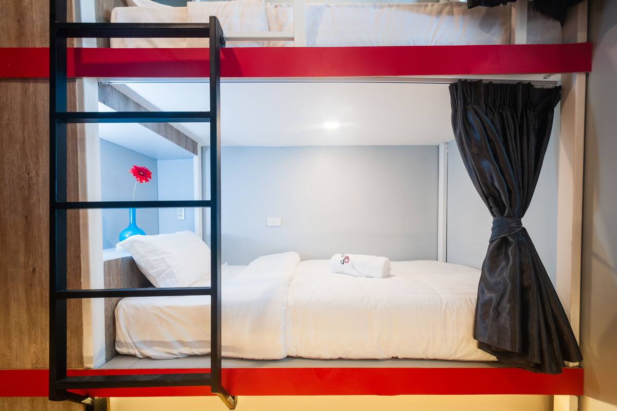 Un lit superposé avec une échelle, du linge de lit blanc et un rideau.