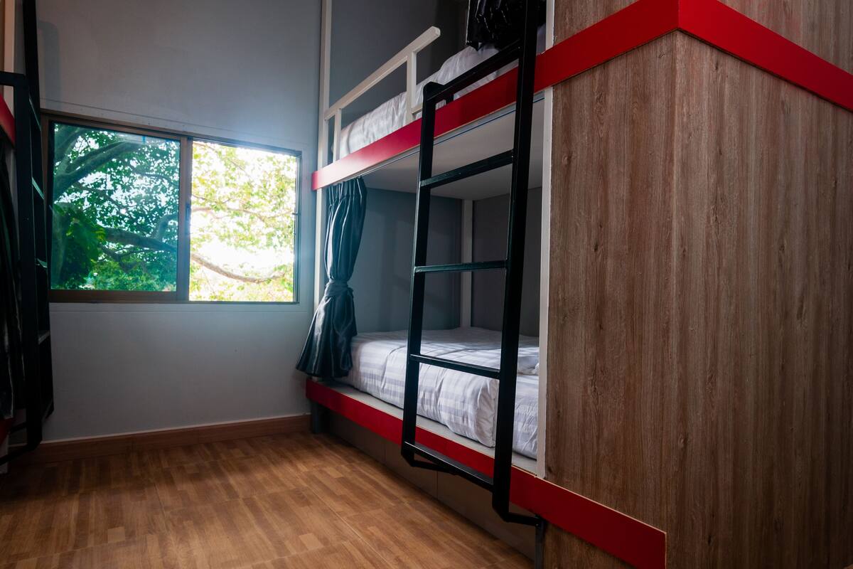 Une chambre avec un lit superposé, une fenêtre, un plancher en bois et un mur d’accent rouge.