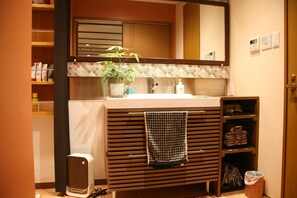 Un baño con tocador de madera, un lavabo, un perchero para toallas, un espejo y una planta en maceta.