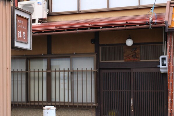 A traditional Japanese building with a sliding door, a signboard, and an air conditioning unit.