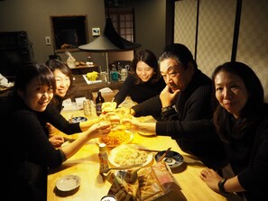 A group of people sitting around a table with food and drinks, in a room with a traditional Japanese aesthetic.