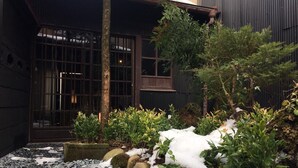 A traditional Japanese-style garden with a stone pathway, snow-covered ground, and a building with large windows and a dark exterior. - Ichii no Niwa (Takayama)
