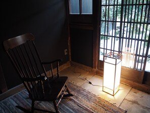 A room with a dark wooden chair, a patterned rug, a standing lamp, and a window with metal bars.