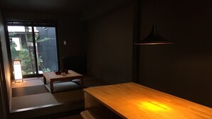 A minimalist dining area with a wooden table and chairs, a small bench, and a sliding glass door leading to a garden. - Ichii no Niwa (Takayama)