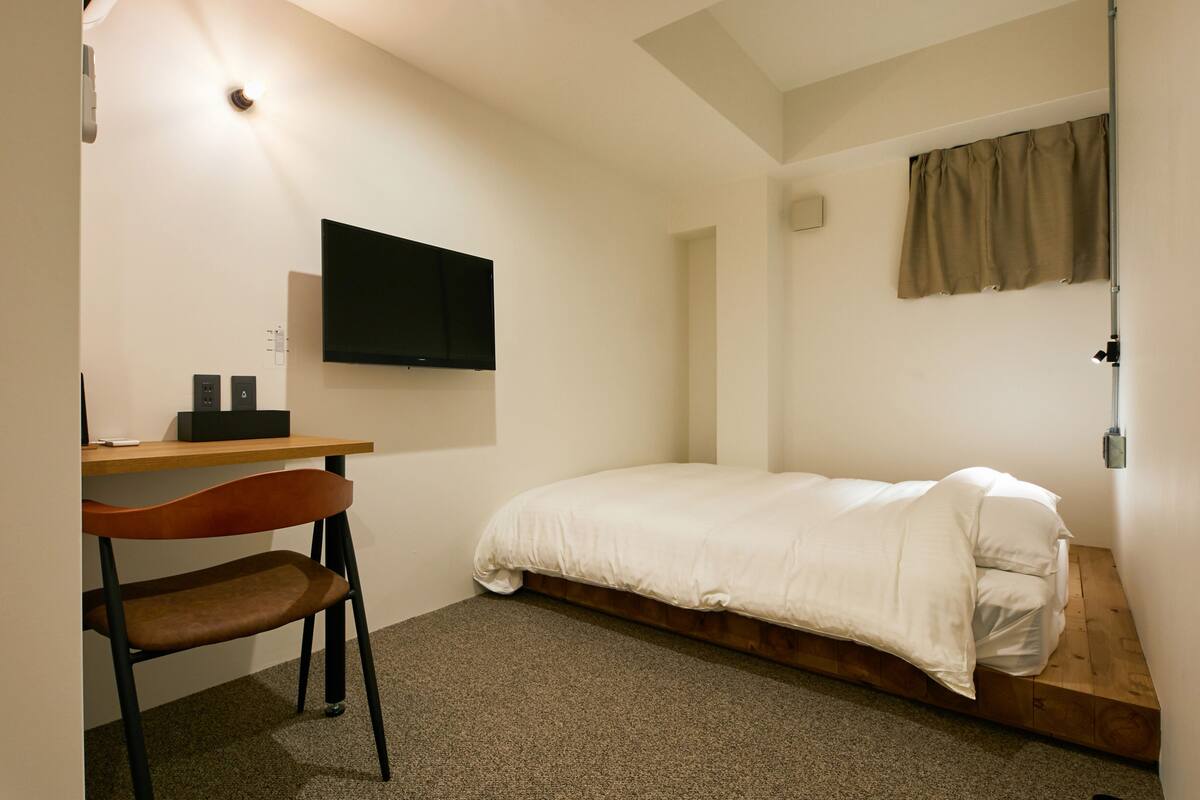 Une petite pièce au décor minimaliste, comprenant un lit, un bureau et une chaise.