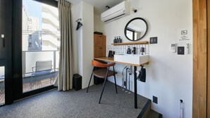 A modern hotel room with a large sliding glass door to a balcony, a wooden desk with a chair, a round mirror, and a white sink. - mizuka Daimyo 7 - unmanned hotel - (Fukuoka)