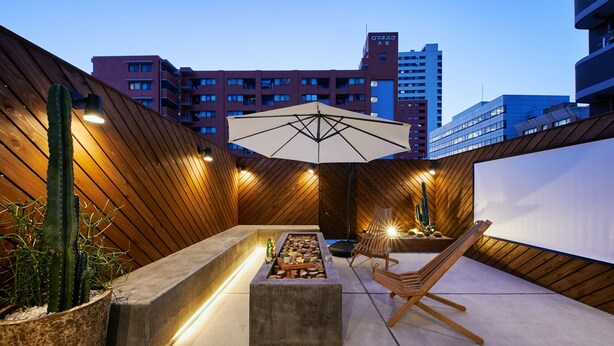 Un espace extérieur aménagé avec des sièges, un foyer, des meubles en bois et un grand parasol.