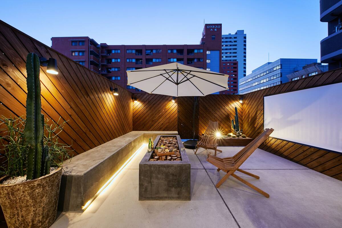 Un espace extérieur aménagé avec des sièges, un foyer, des meubles en bois et un grand parasol.