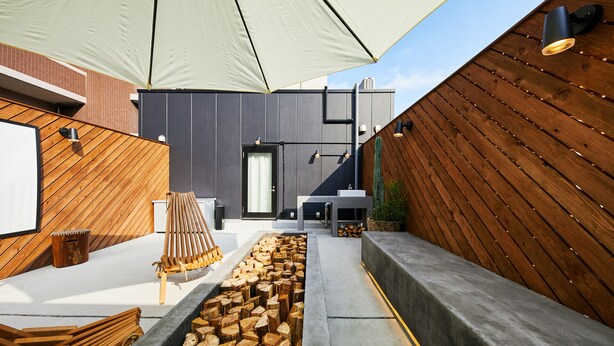 A modern outdoor seating area with a wooden bench, a fire pit, and a large umbrella providing shade. - mizuka Daimyo 7 - unmanned hotel - (Fukuoka)