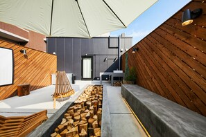 Un espace extérieur moderne, aménagé avec un banc en bois, un foyer et un grand parasol pour créer de l’ombre.