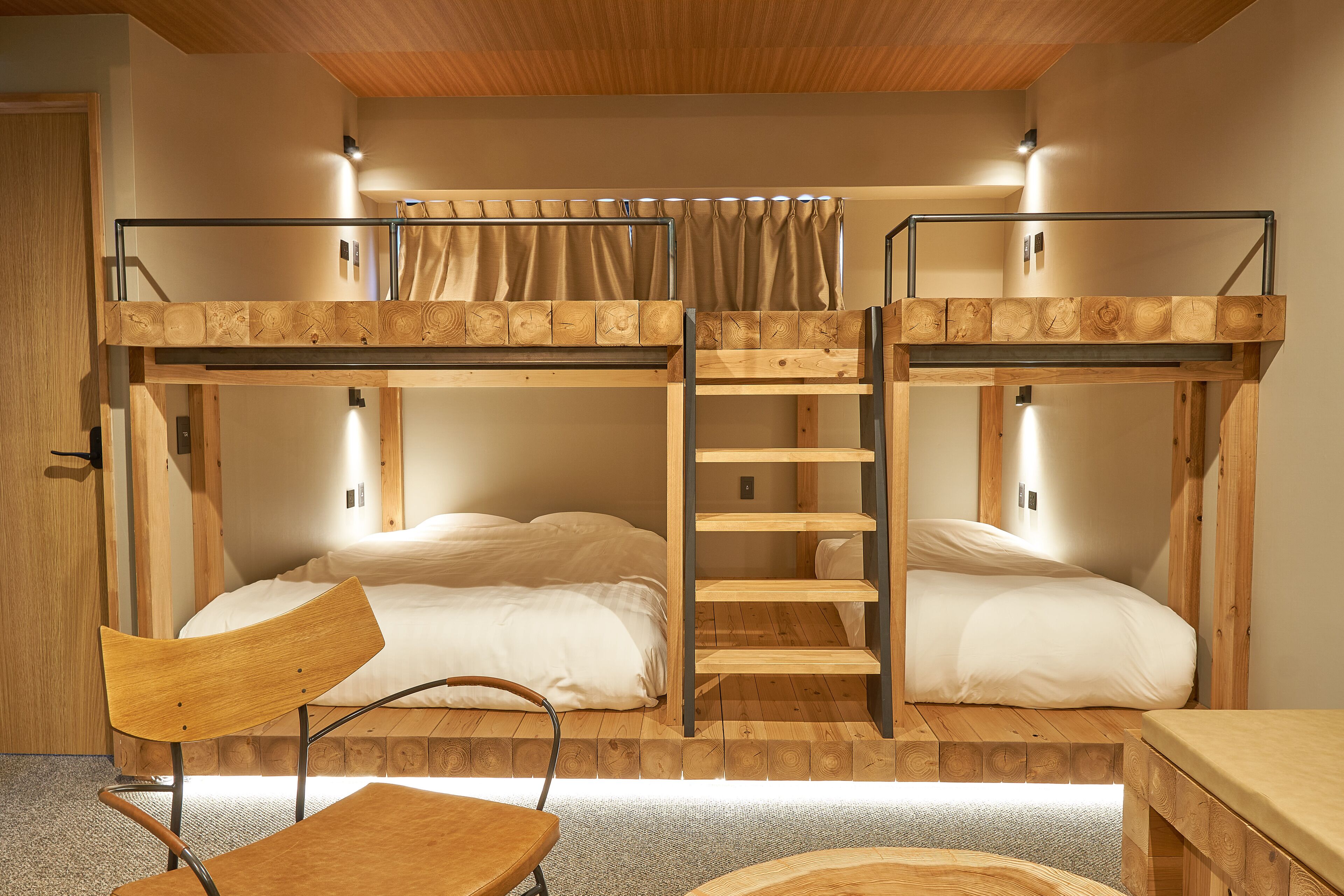 A bunk bed room with a wooden ladder, a chair, and a small table.