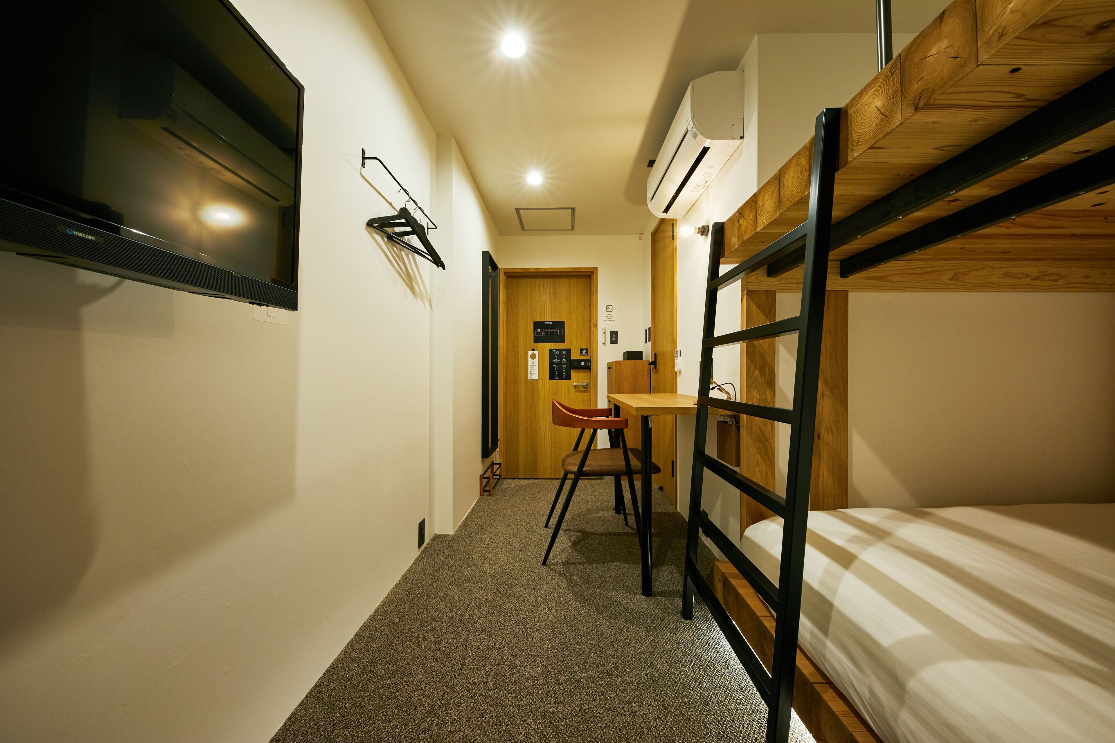 A compact room with a bunk bed, a desk with a chair, a flat-screen TV mounted on the wall, and an air conditioning unit.
