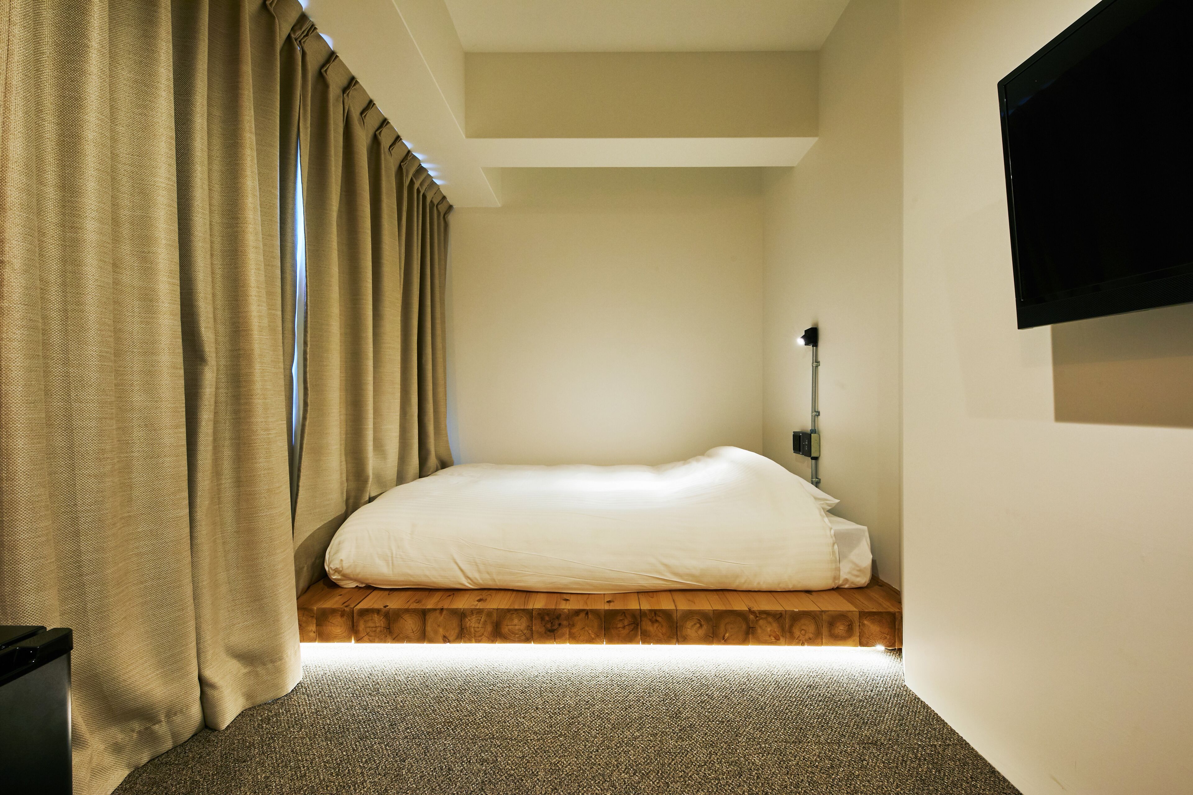 A bedroom with a bed, curtains, a TV, and a wooden platform.