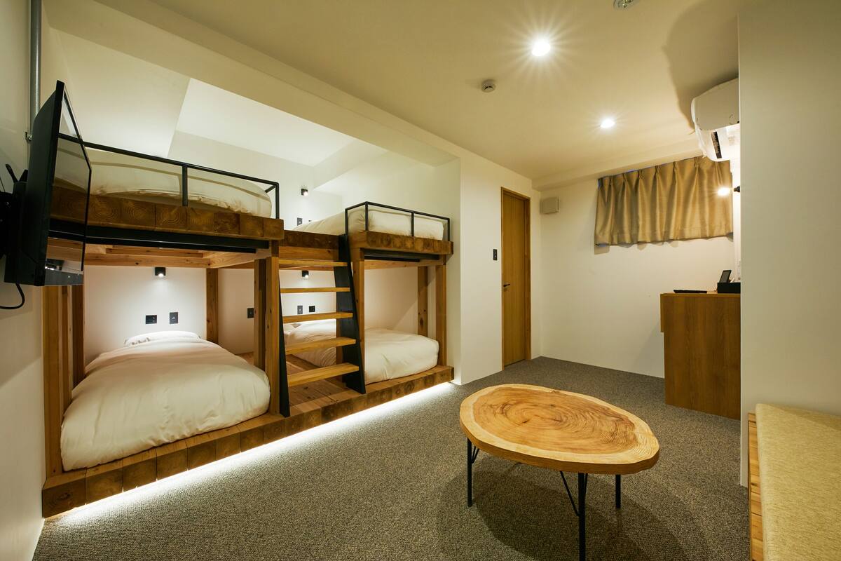 Une pièce avec des lits superposés, une table ronde en bois et un petit bureau.