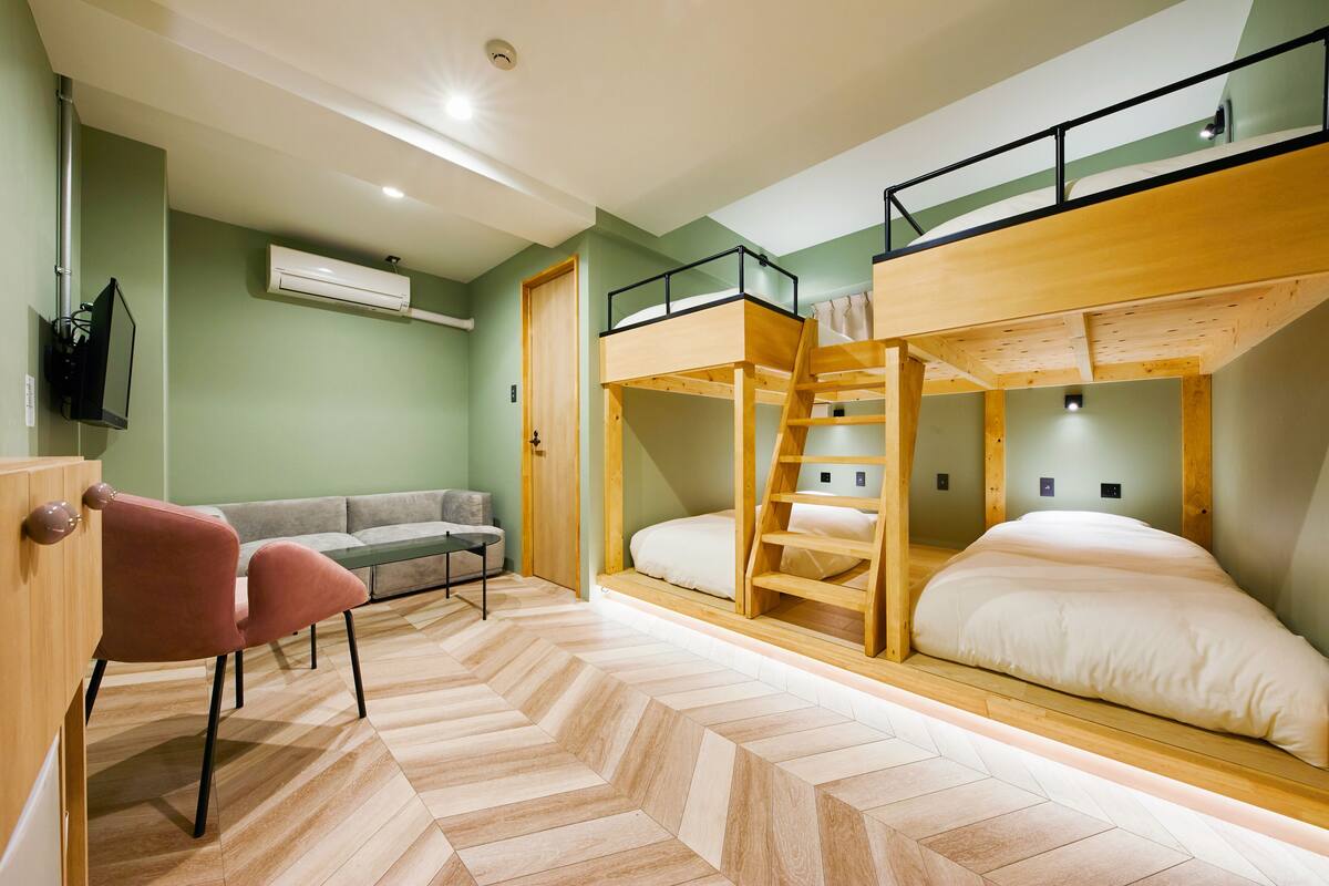 Une pièce comprenant un lit superposé, un canapé, une chaise et un bureau en bois.