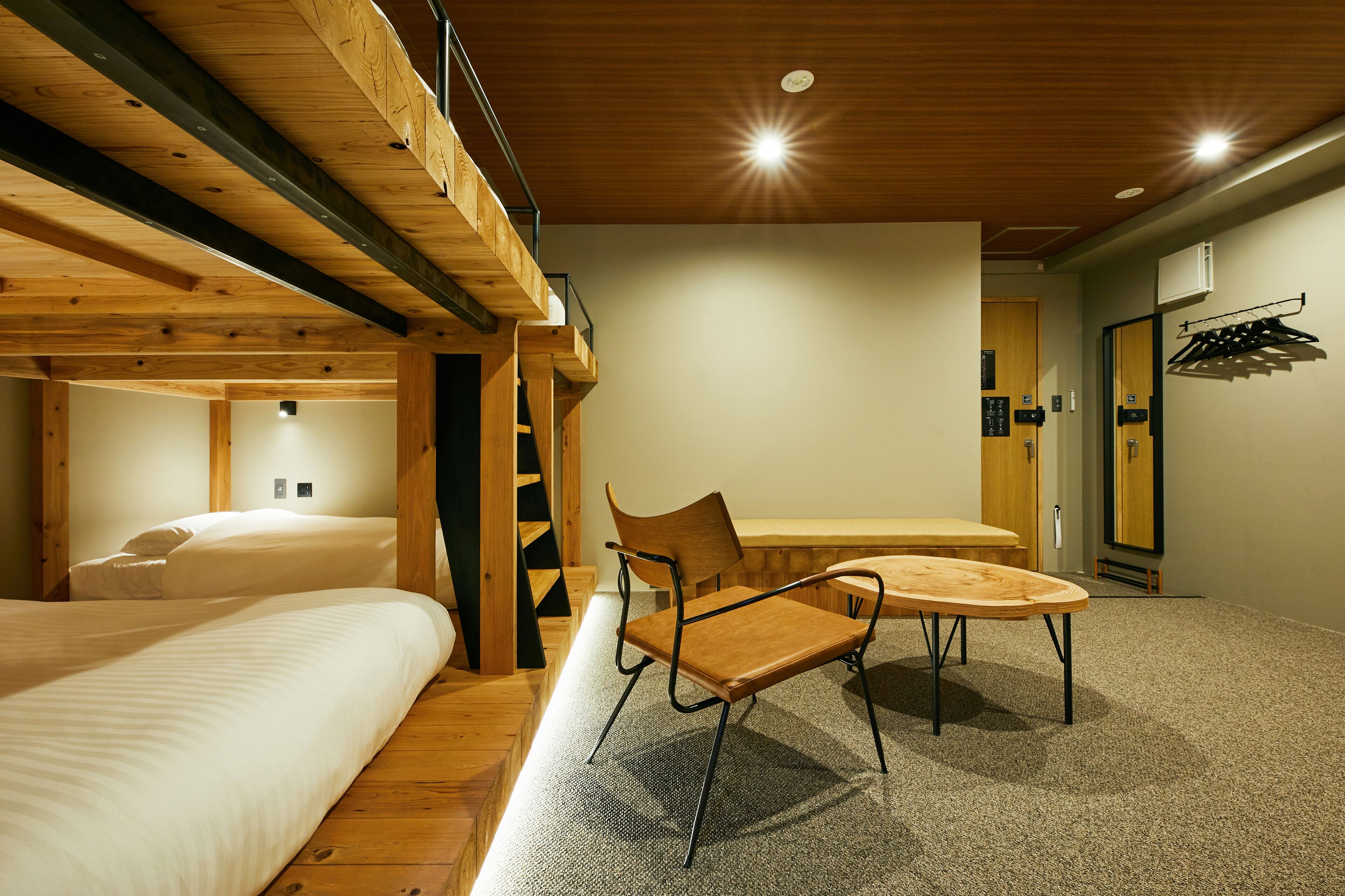 Una habitación con dos camas, una mesa de madera, una silla y un banco.