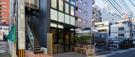 A modern building with a black facade, large windows, and a visible entrance with a staircase.