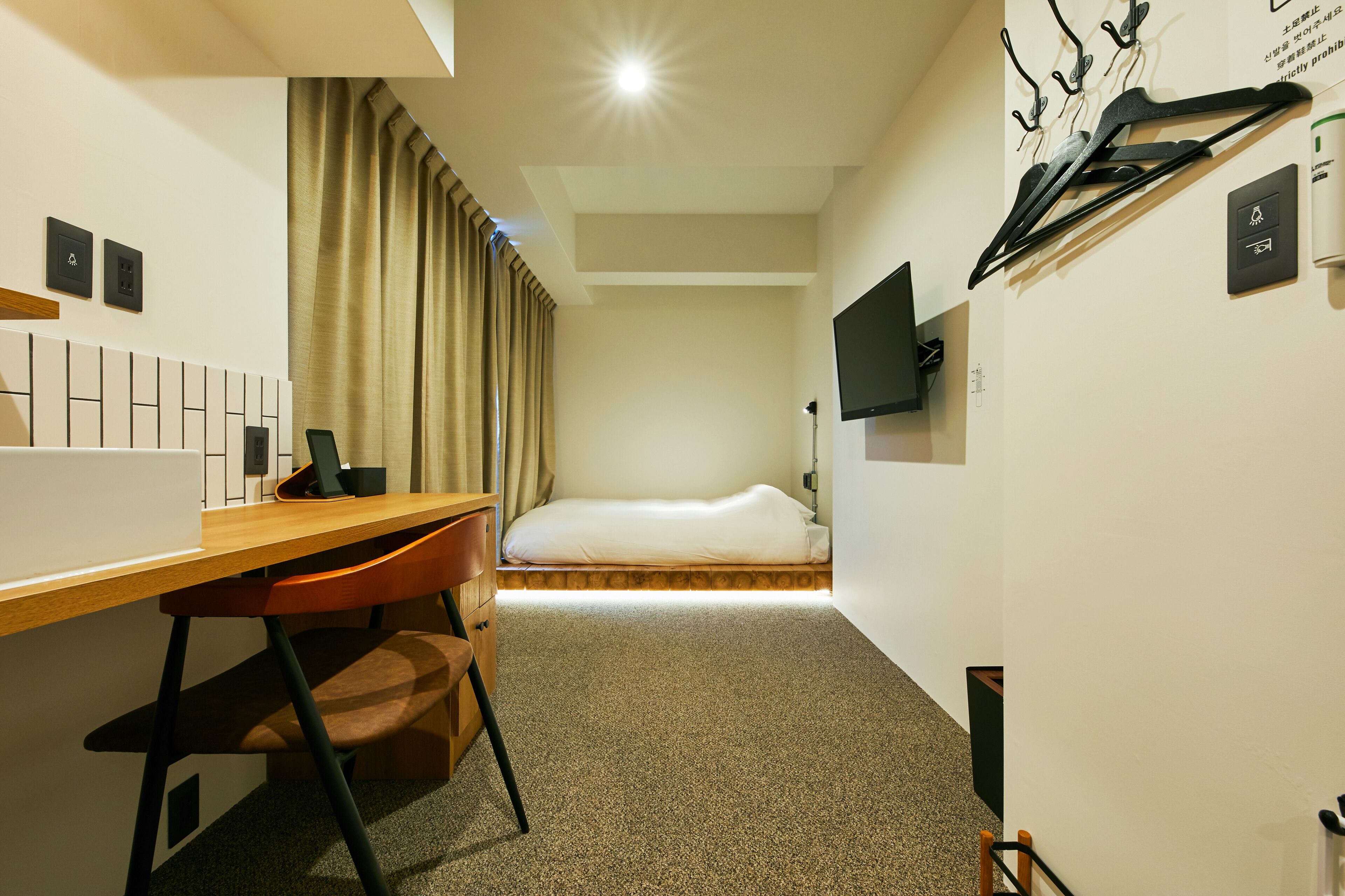Camera d'albergo compatta con un letto singolo, una scrivania con sedia, una TV a parete e un appendiabiti.