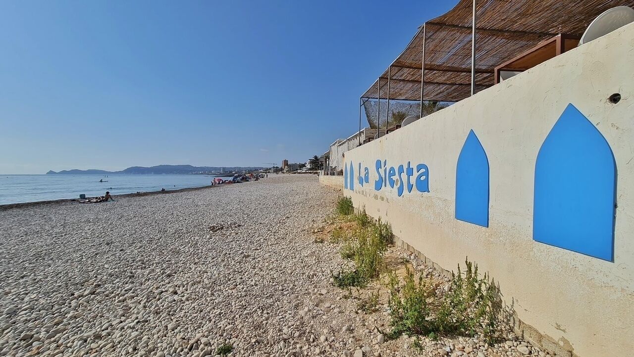 Un hôtel situé en bord de mer, offrant une vue dégagée sur l’océan, avec une plage de galets et une enseigne indiquant « La Siesta ».