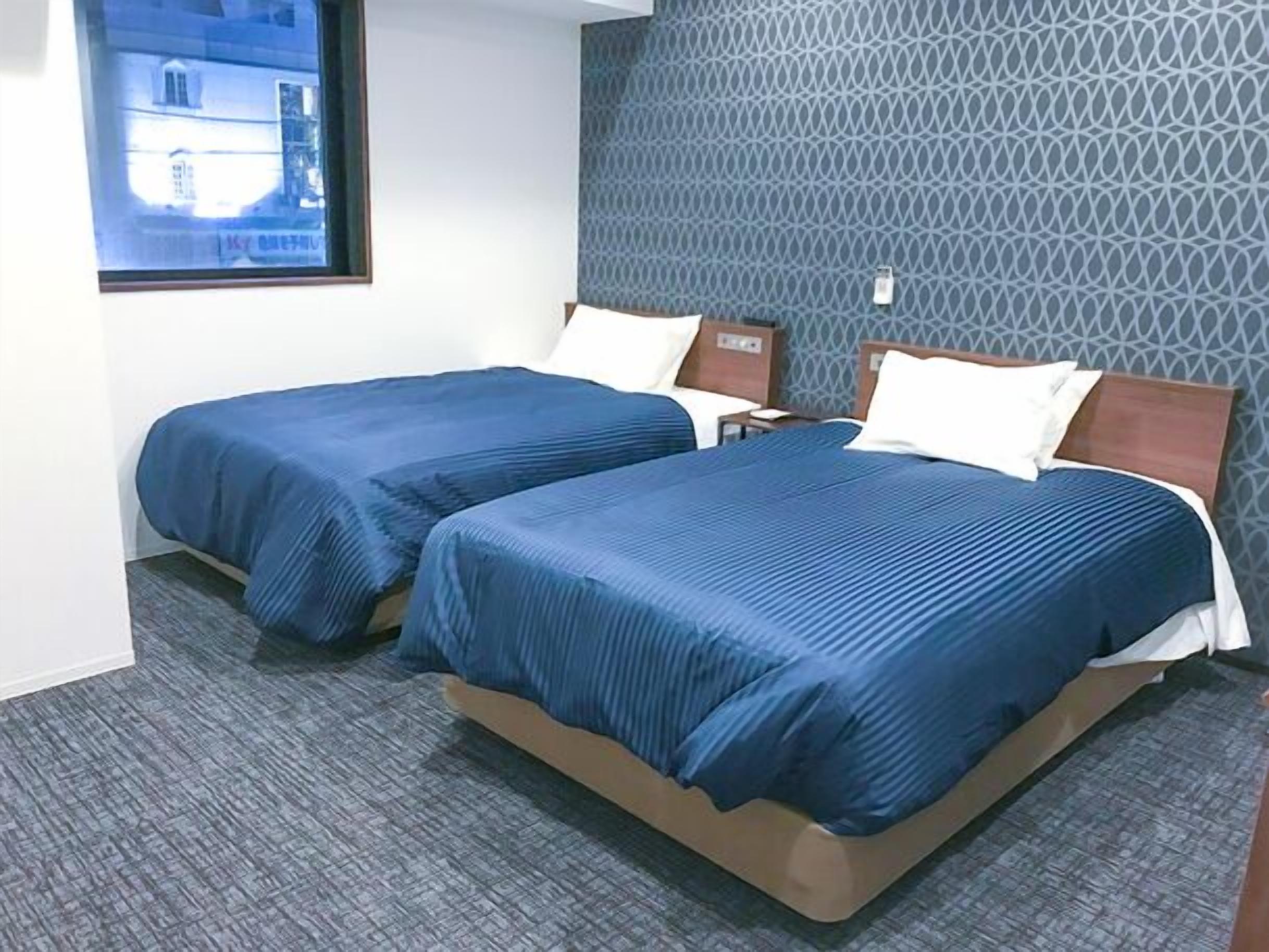 A hotel room with two beds, a patterned wall, and a window with a view.