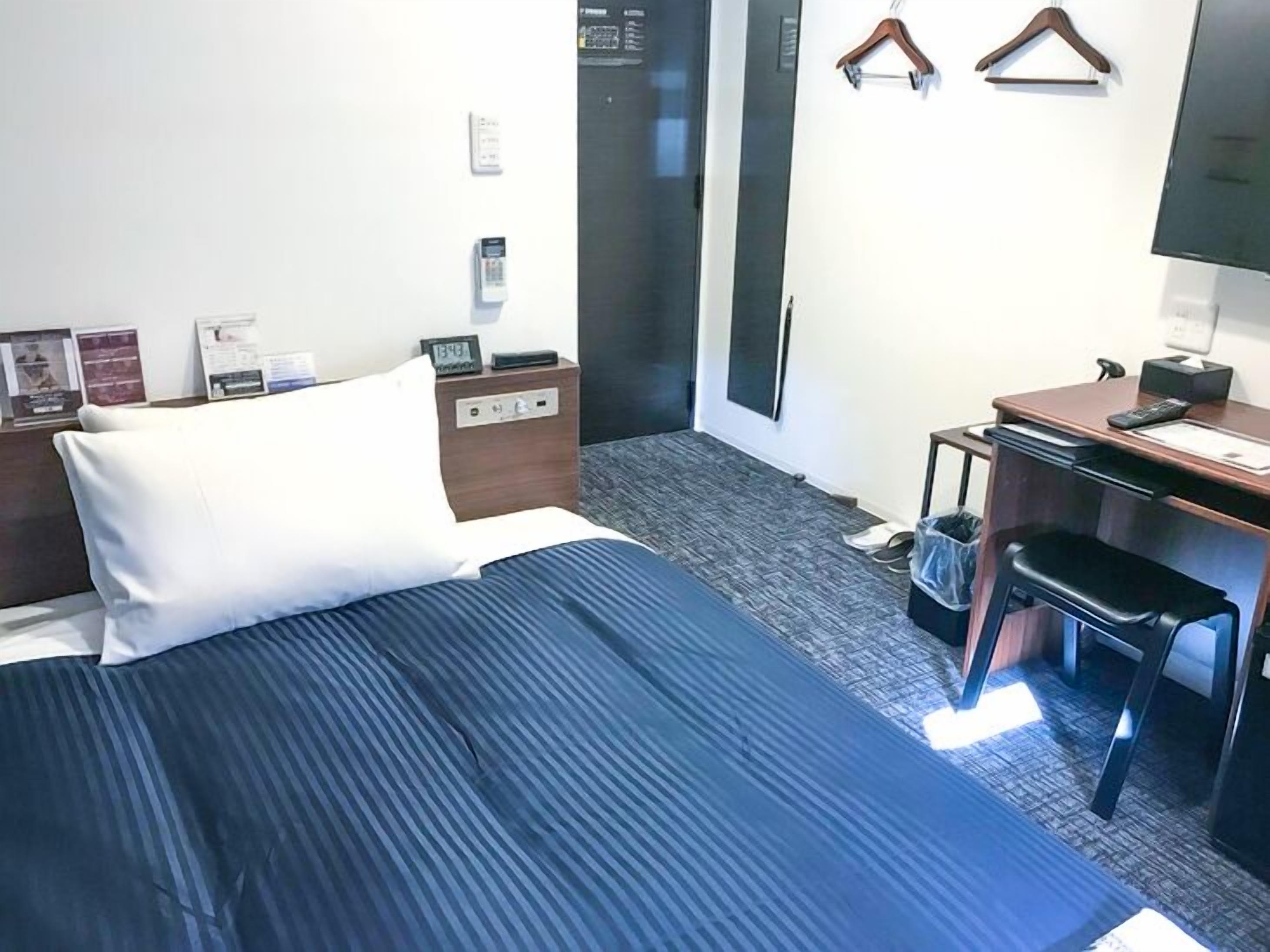 A hotel room with a bed, a desk, a chair, a wardrobe, and a TV.