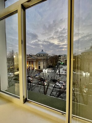 Blick durch ein Fenster auf ein Gebäude mit einer Kuppel, einen Parkplatz und eine Straße mit Autos und kahl stehenden Bäumen.
