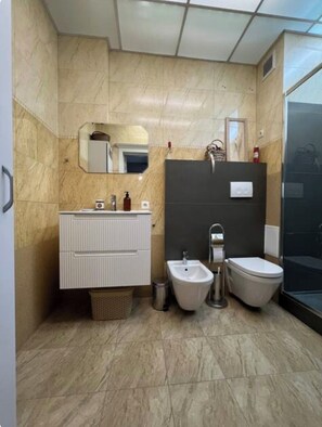 Une salle de bain moderne avec un sol en marbre, un meuble-lavabo blanc doté d’un miroir, un bidet et des toilettes.