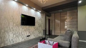 Ein modernes Wohnzimmer mit einem grauen Sofa, einem flachbildfernseher an einer strukturierten Wand und einem Kronleuchter.