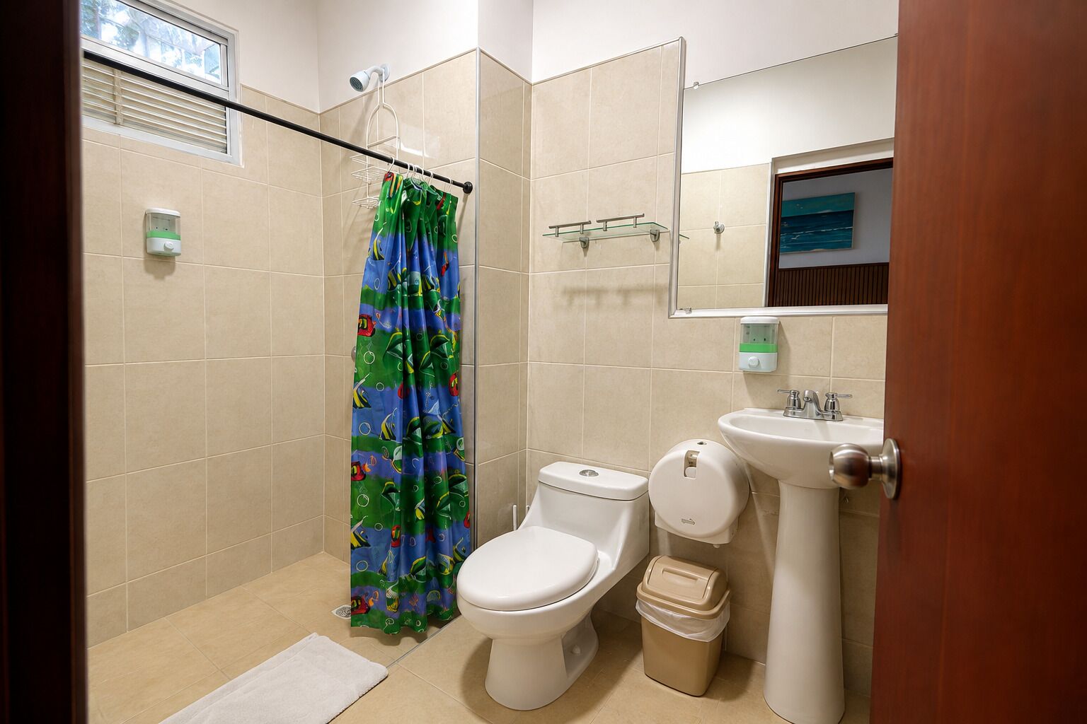 A bathroom with a shower, toilet, sink, and a trash bin.