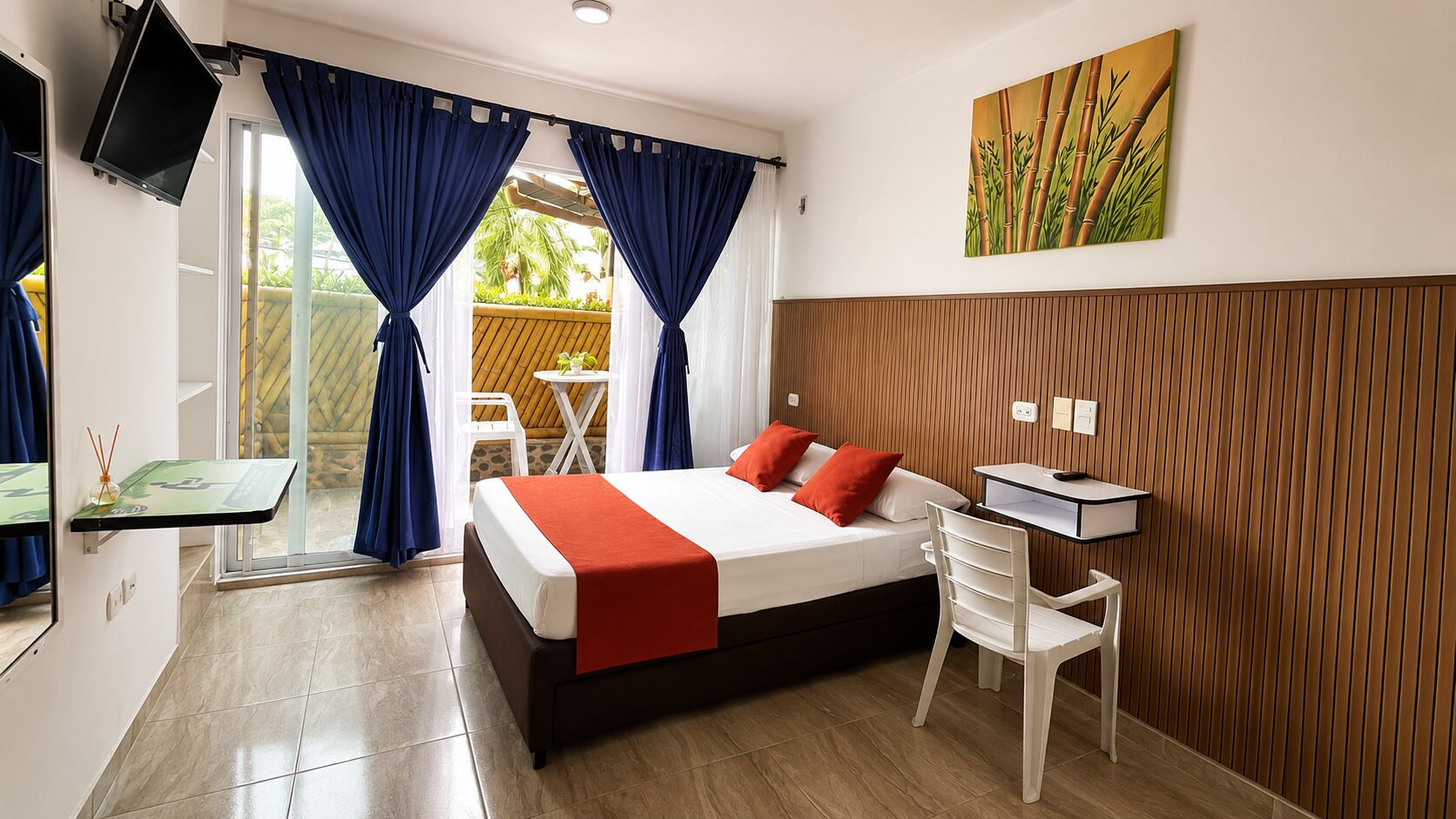 A hotel room with a bed, a desk, a chair, a TV, and a painting on the wall.